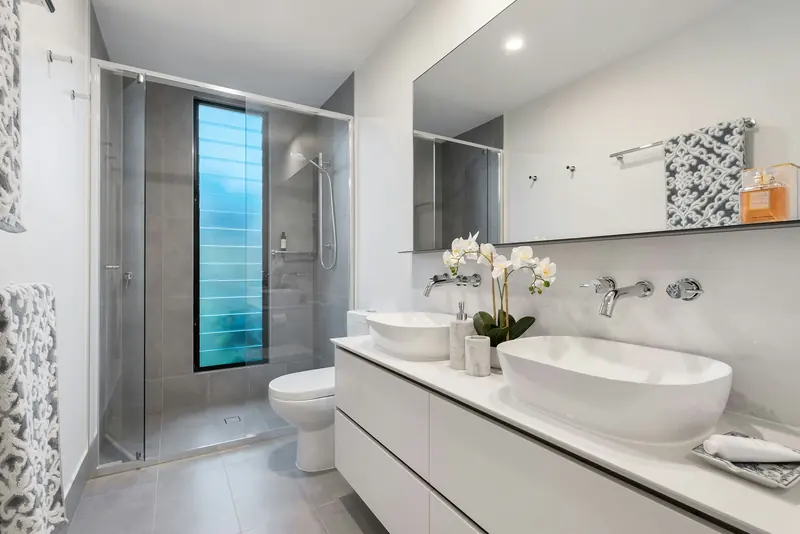 Baño luminoso con mueble de lavabo blanco y mampara de cristal