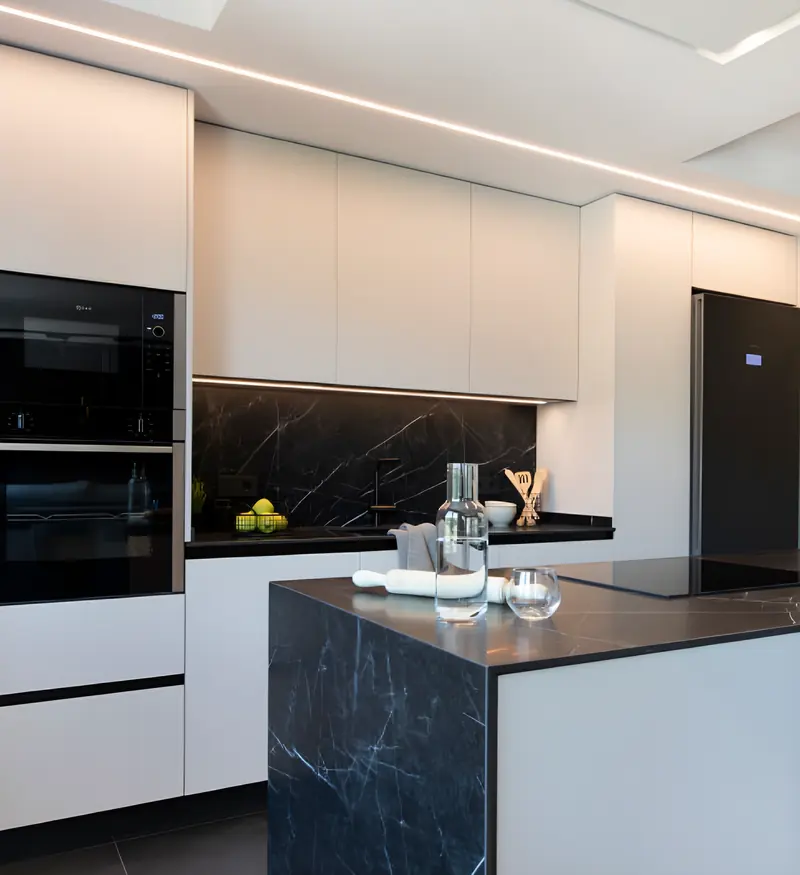 Cocina reformada con muebles blancos sin tiradores, isla y encimera negra veteada