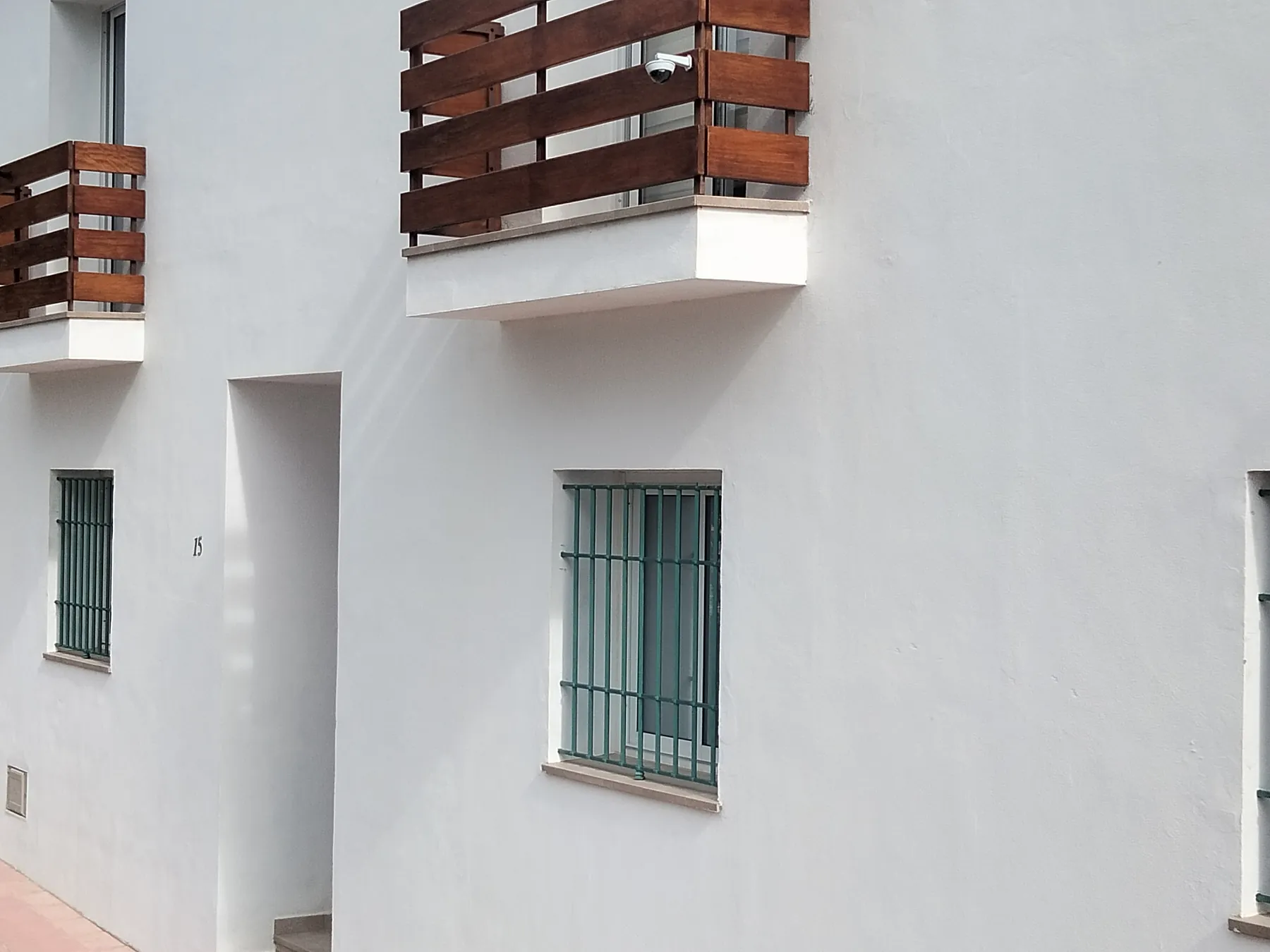 Fachada blanca recién terminada con balcones de madera y rejas verdes