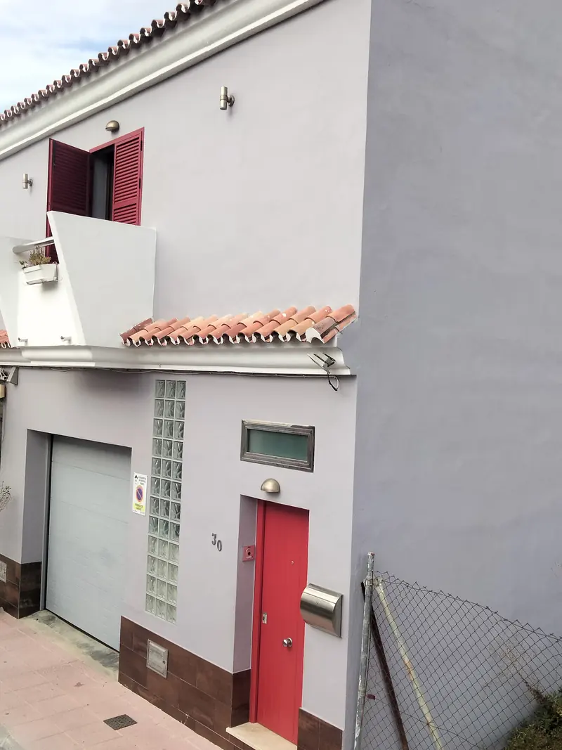 Fachada pintada con zócalo marrón, puerta roja y cochera